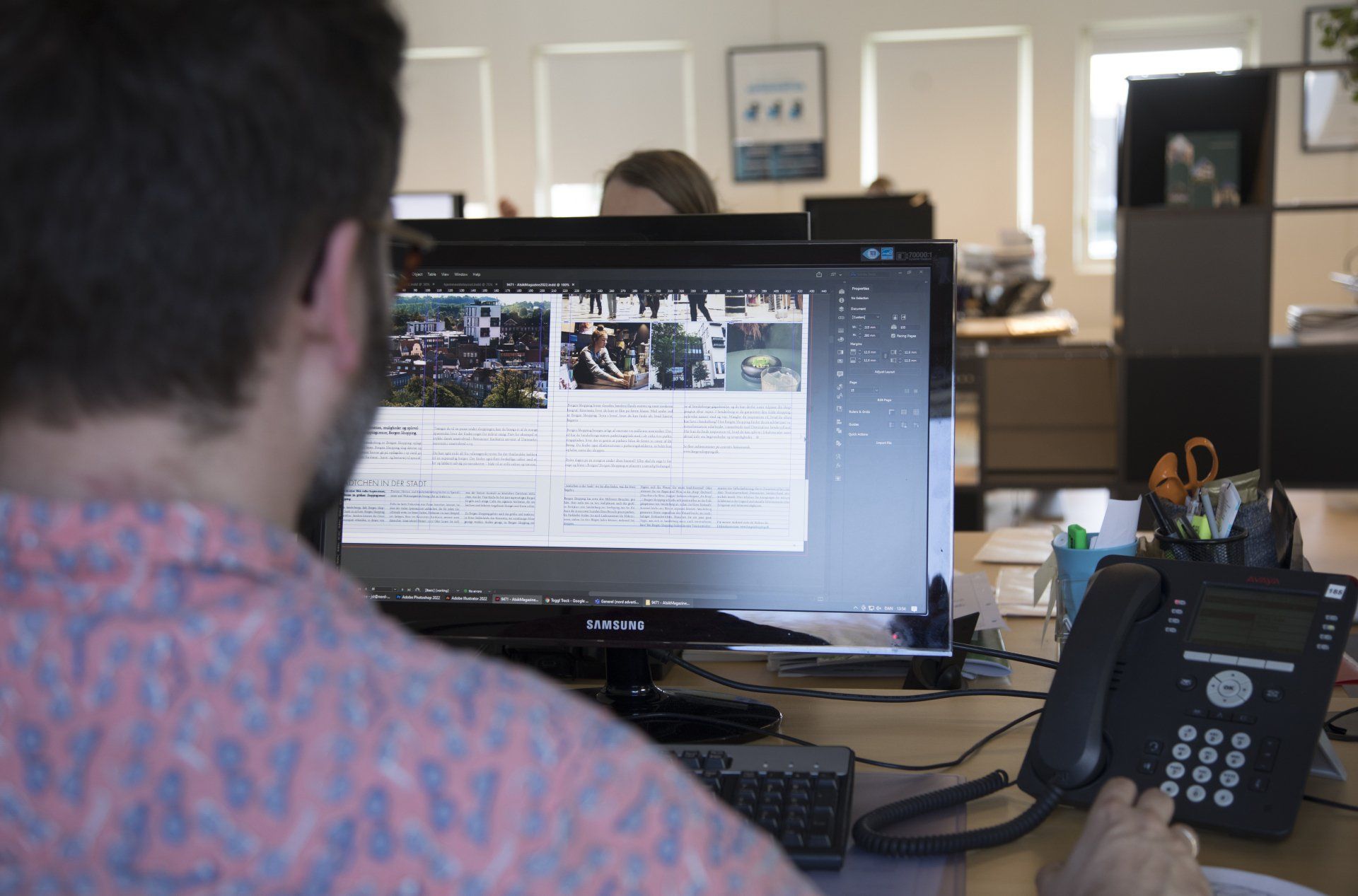 En medarbejder, der sidder ved en computerskærm. Skærmen viser programmet InDesign, hvor han layouter brandingmateriale og visuelle identiteter.