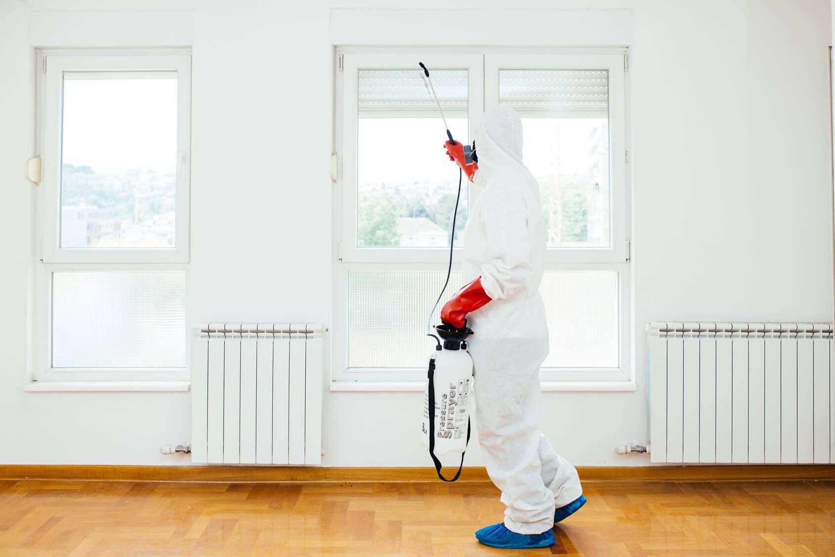 A person in a protective suit is spraying a room with a sprayer.
