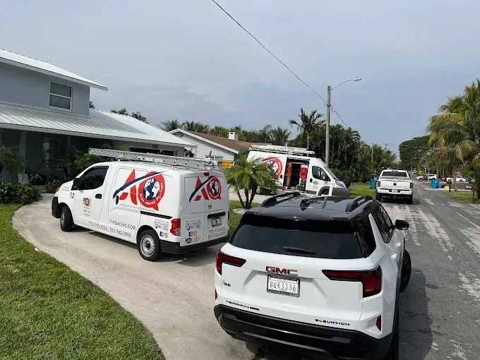 Two white AC service vans parked in a residential driveway next to a white SUV on a sunny day.