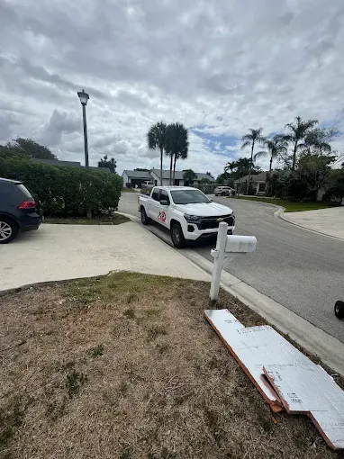 A white service pickup truck parked on the side of a suburban street next to a mailbox and a pile of discarded material.