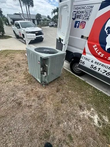 A white service van parked on grass with a detached air conditioning condenser unit standing on the ground beside it.