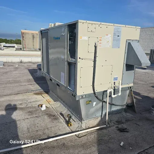 A large, beige industrial HVAC rooftop unit sits on a flat, gray commercial roof under a clear blue sky.