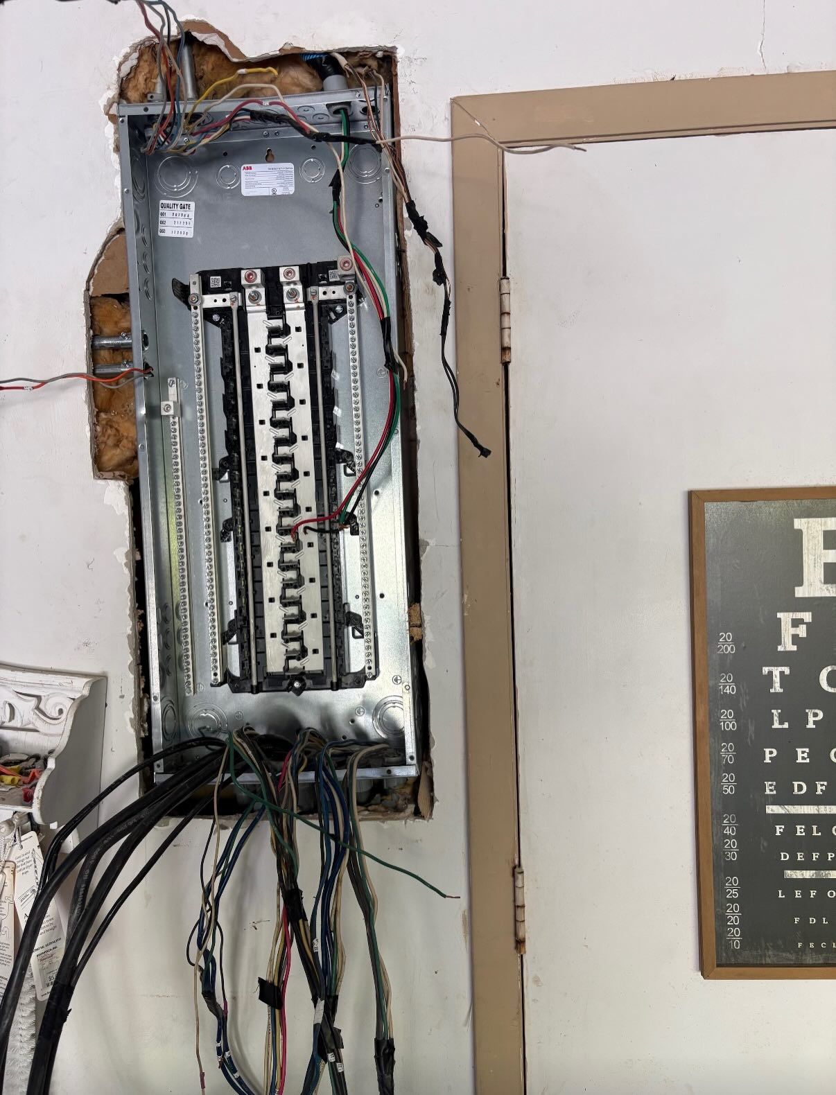 An open electrical breaker panel mounted on a wall next to a door frame and an eye chart.