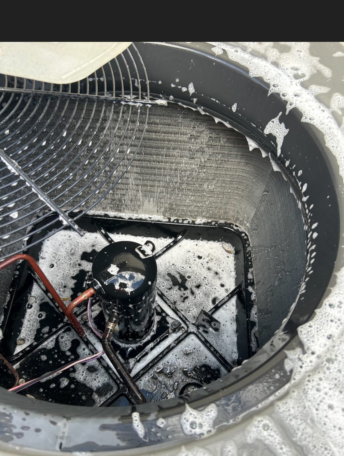A top-down view of an outdoor HVAC unit undergoing maintenance, with foaming cleaning solution covering the components.