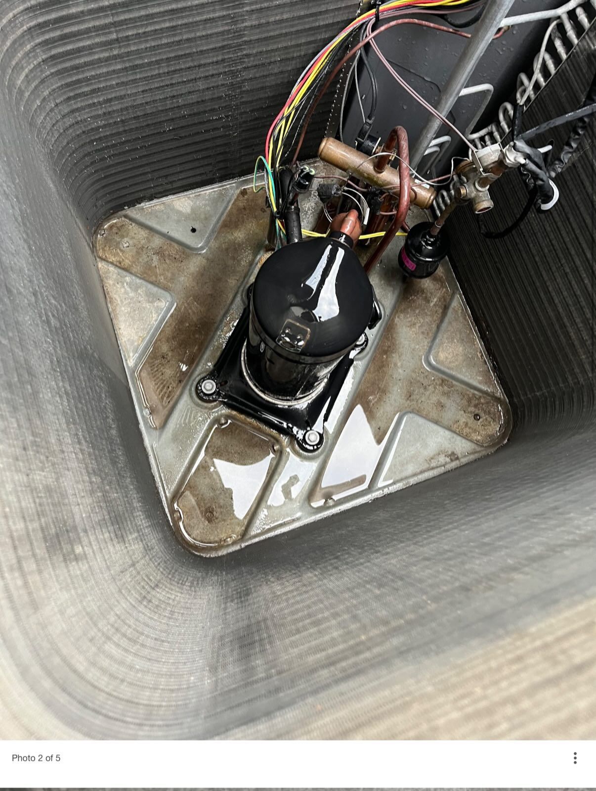 High-angle view of a black compressor unit inside an air conditioning system's metal housing with visible condensation.
