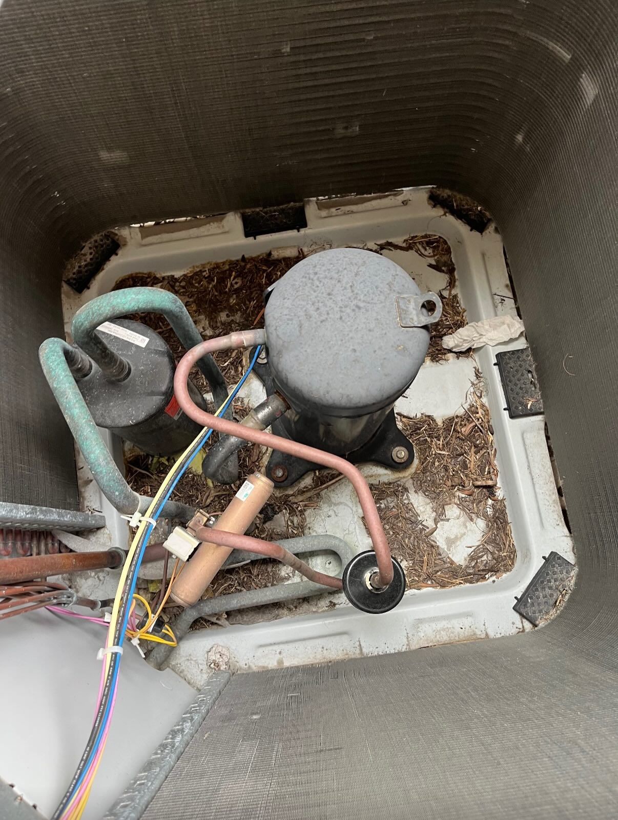 High-angle view inside an outdoor air conditioner unit showing the compressor and debris on the base pan.