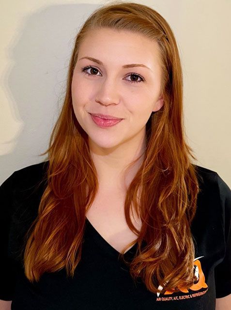 A person with long, reddish-brown hair smiling at the camera, wearing a black v-neck shirt against a plain background.