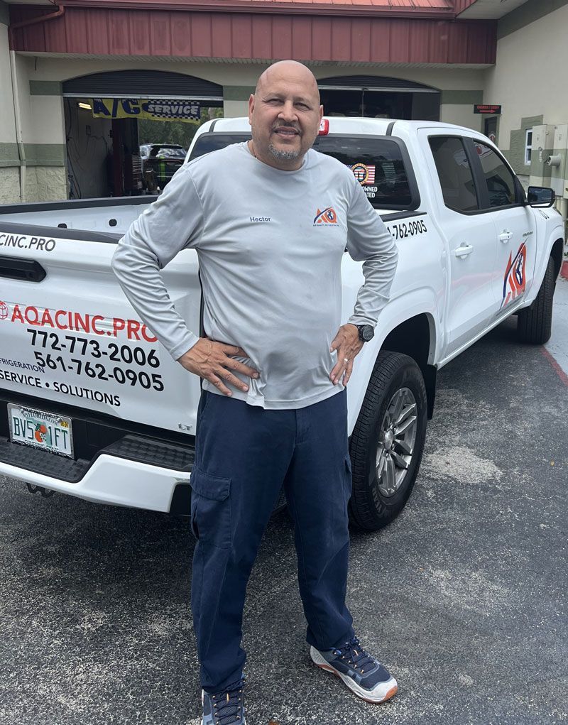 A man in a gray long-sleeved shirt and blue pants standing in front of a white work truck.