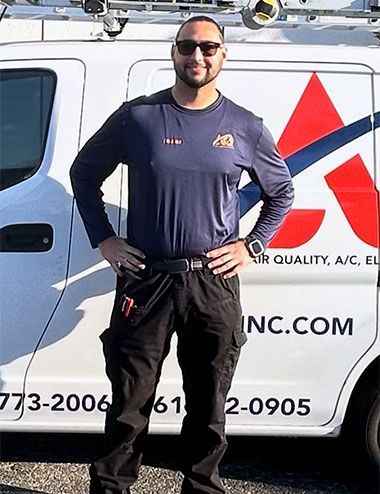 A technician in a navy shirt and black work pants stands smiling with hands on hips in front of a company service van.