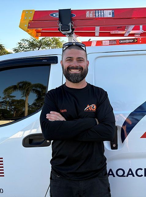 A smiling professional in a black long-sleeve shirt stands with arms crossed in front of a white work van with a ladder.