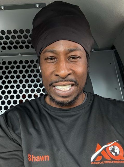 A smiling person wearing a black head covering and a black long-sleeved shirt with the