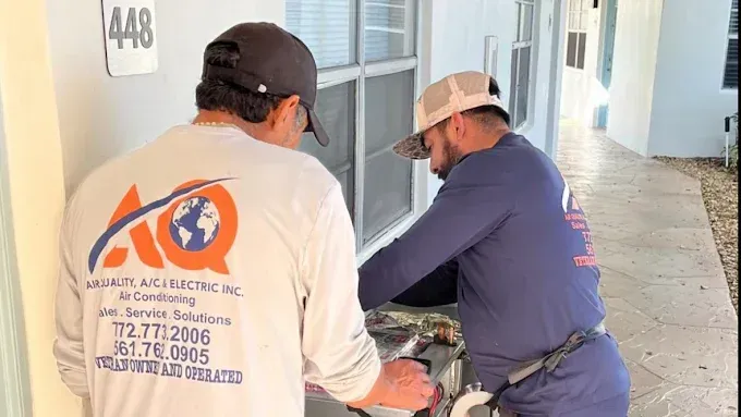 Two technicians in long-sleeved work uniforms perform maintenance on equipment outside apartment 448.