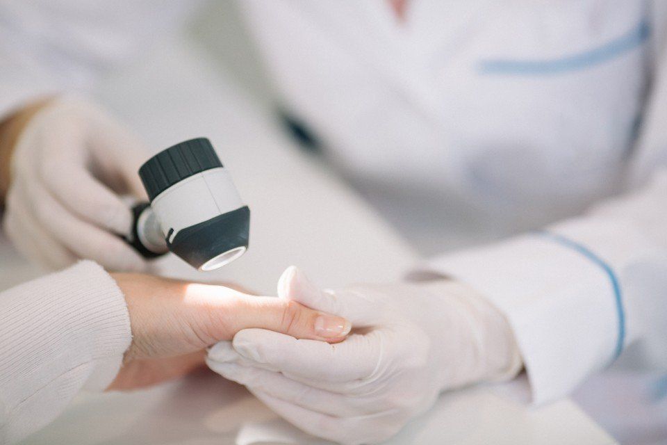 Un dermatologo che esamina la mano di una paziente con un dermatoscopio