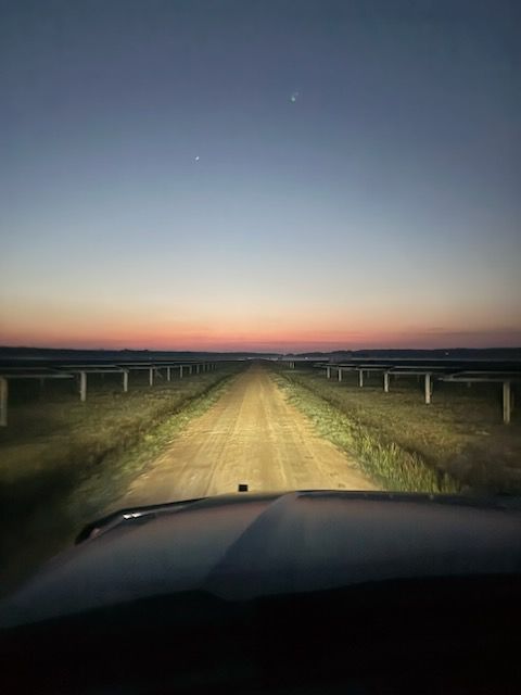 Aerial view: roads intersect, dividing green fields and a forest with some cleared land visible.