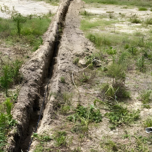 A long, narrow trench dug in a grassy field, possibly for laying cables or pipes.