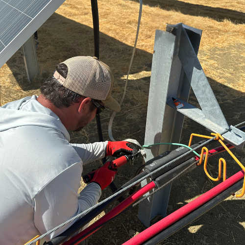 A machine pulling a large cable spool across a grassy field, with solar panels visible in the background.