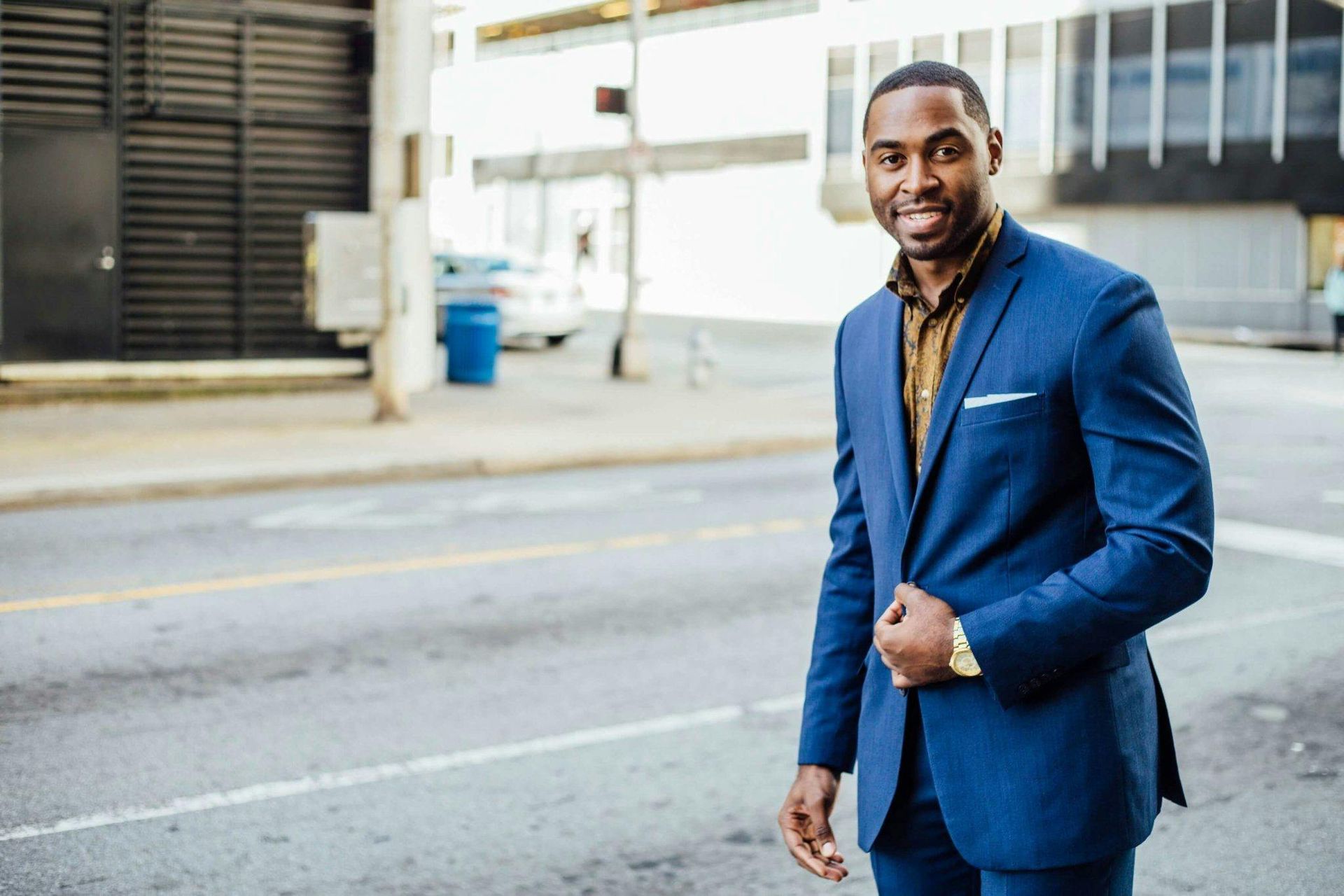 Man in blue suit smiling on a city street.