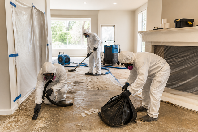 Workers in white suits cleaning debris in a renovated room with plastic-covered walls and floor.