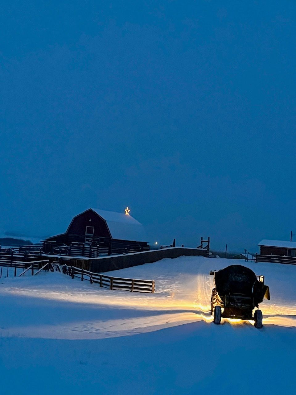 A snowmobile is driving through a snowy field with a barn in the background
