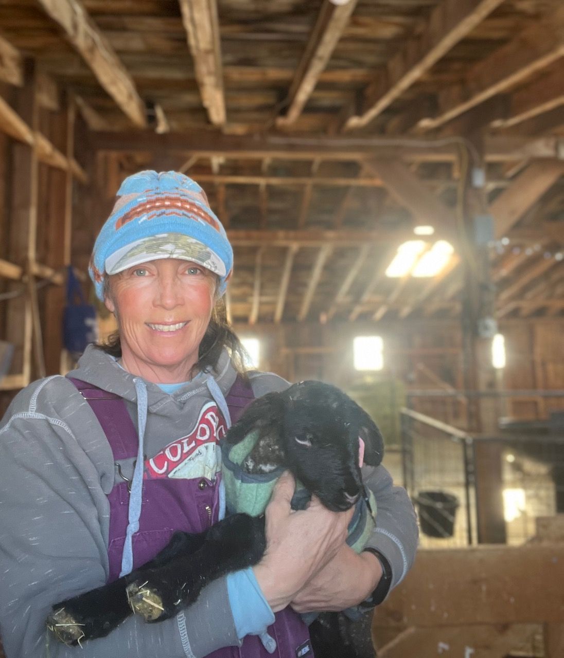 Marcy is holding a puppy in her arms in a barn.