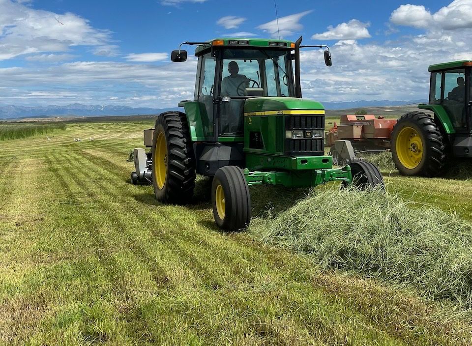 A john deere tractor is cutting north park grass hay in a field