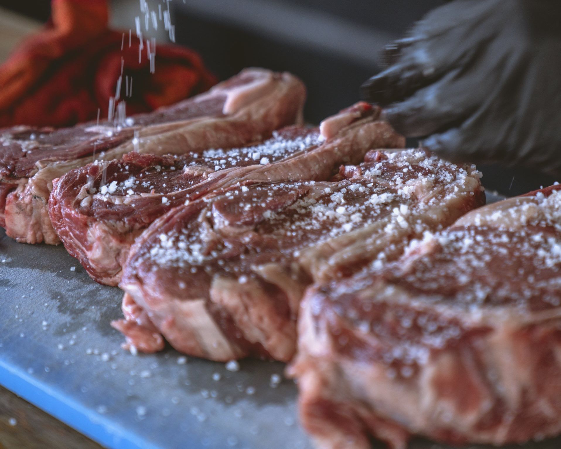 A person is sprinkling salt on a gras fed steak on a cutting board.
