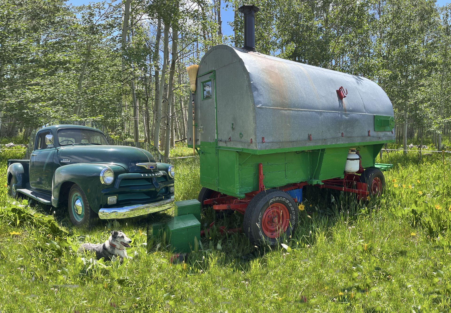 A green truck and a green trailer are parked in a grassy field.