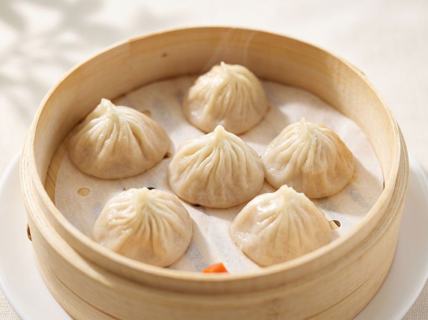 Steamed dumplings in a bamboo basket on a white plate