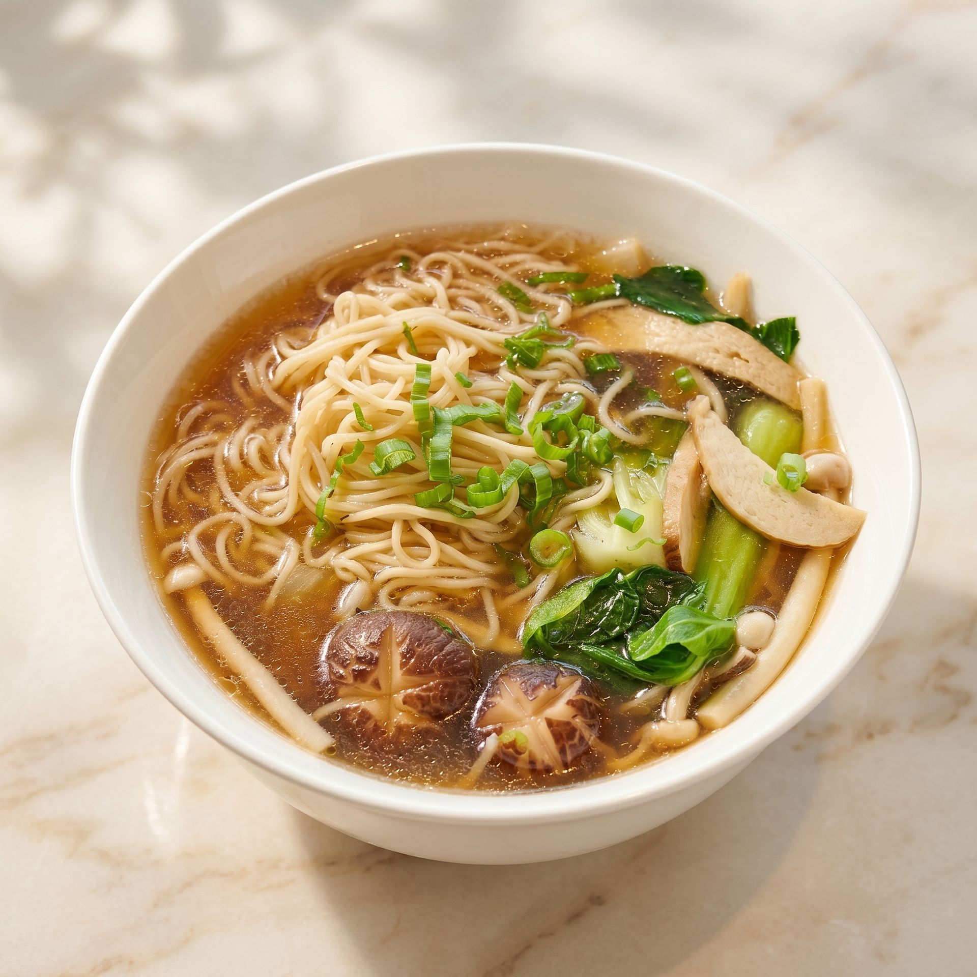 Bowl of noodle soup with mushrooms, greens, and shredded toppings on a light marble table