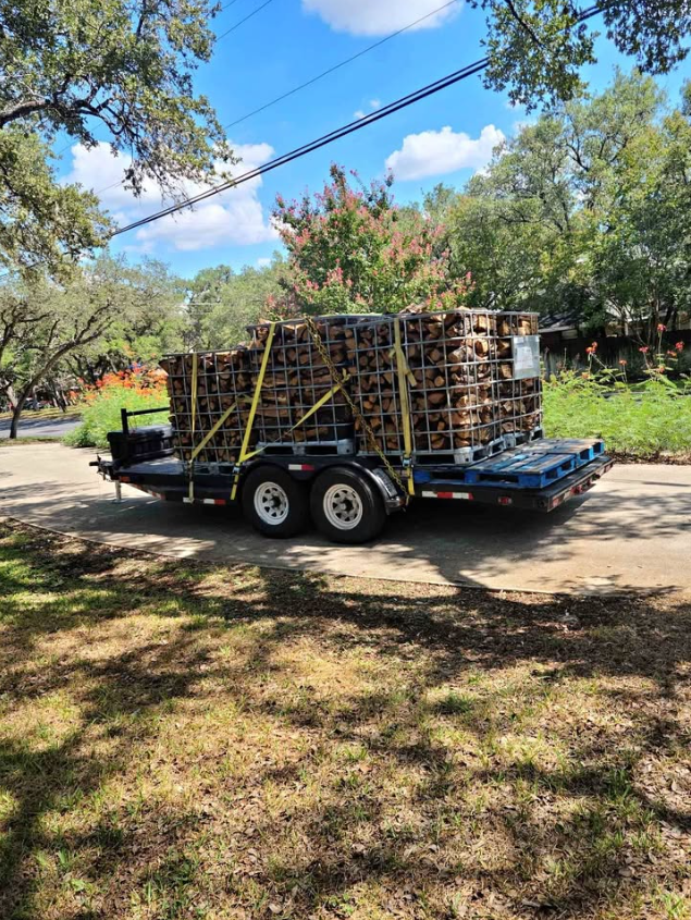 Trailer loaded with stacks of wooden crates secured with yellow straps, parked on a grassy area.
