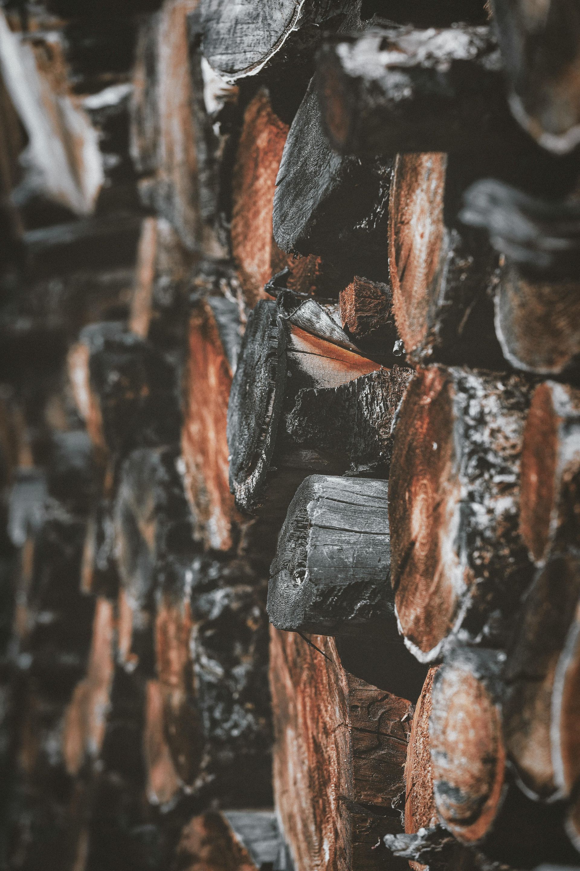 Pile of stacked firewood, showing rough-cut logs with reddish-brown and gray coloring.