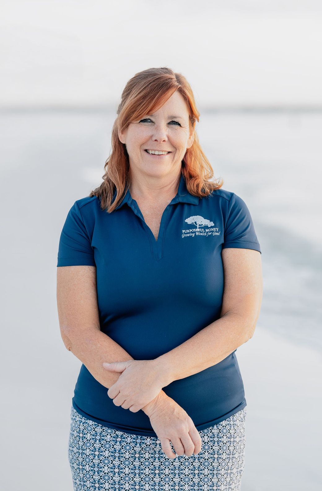 A woman with red hair is smiling and wearing a white shirt.