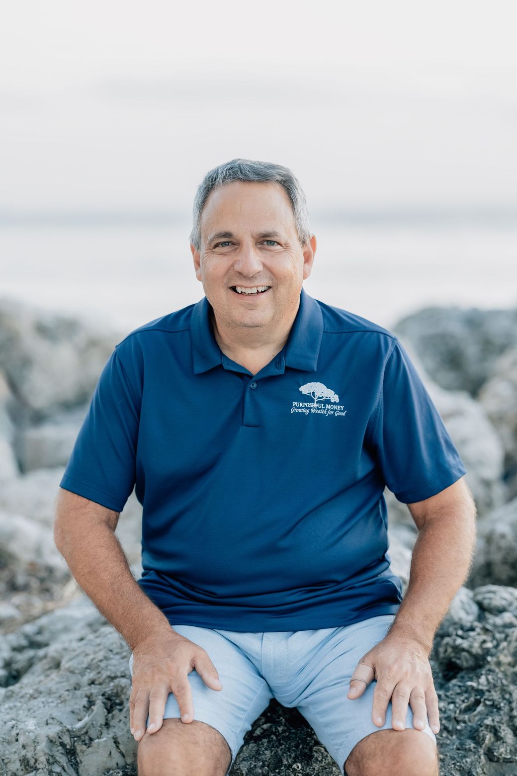 A man in a black polo shirt is standing in front of a bush.