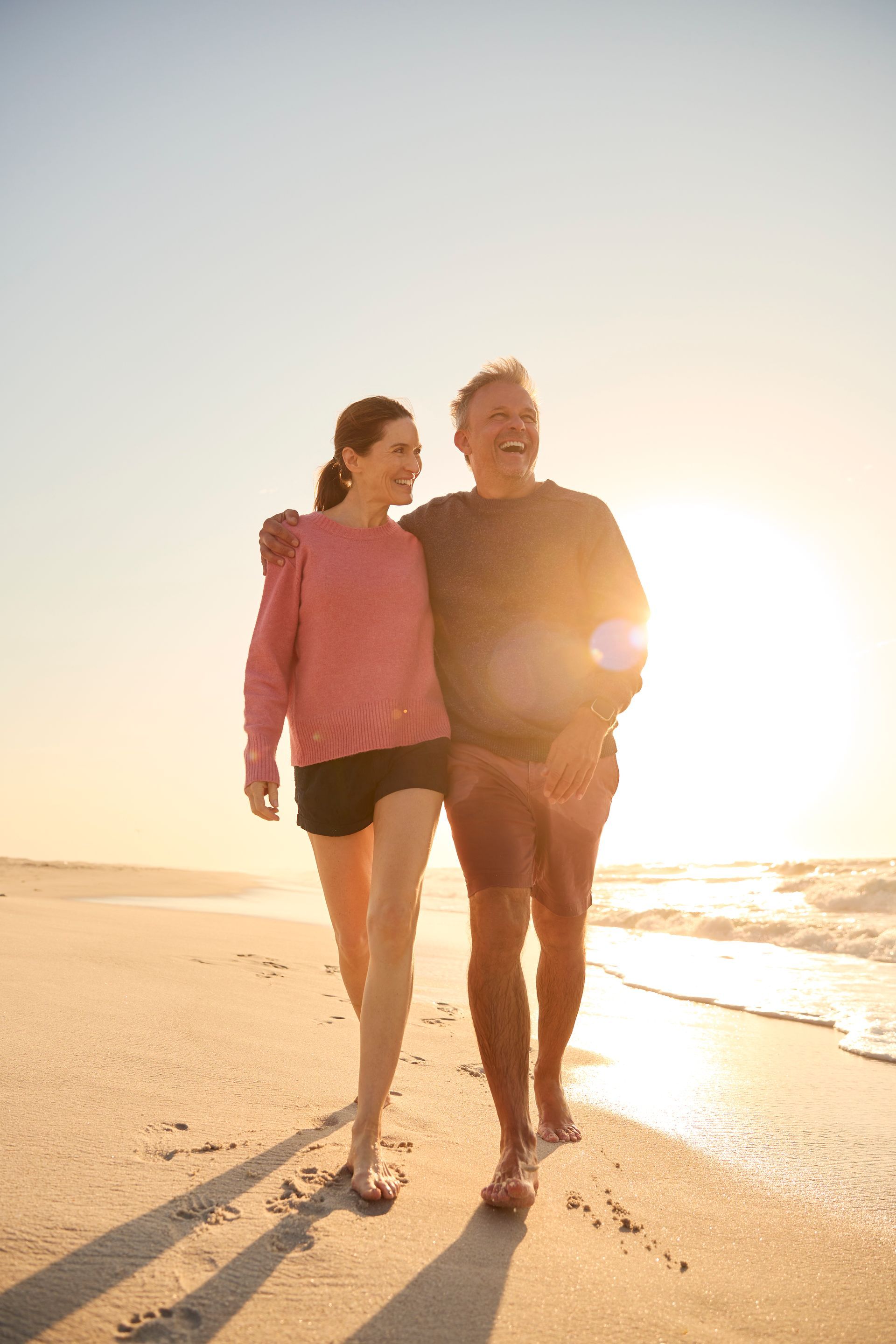 A man and a woman are walking on the beach at sunset.