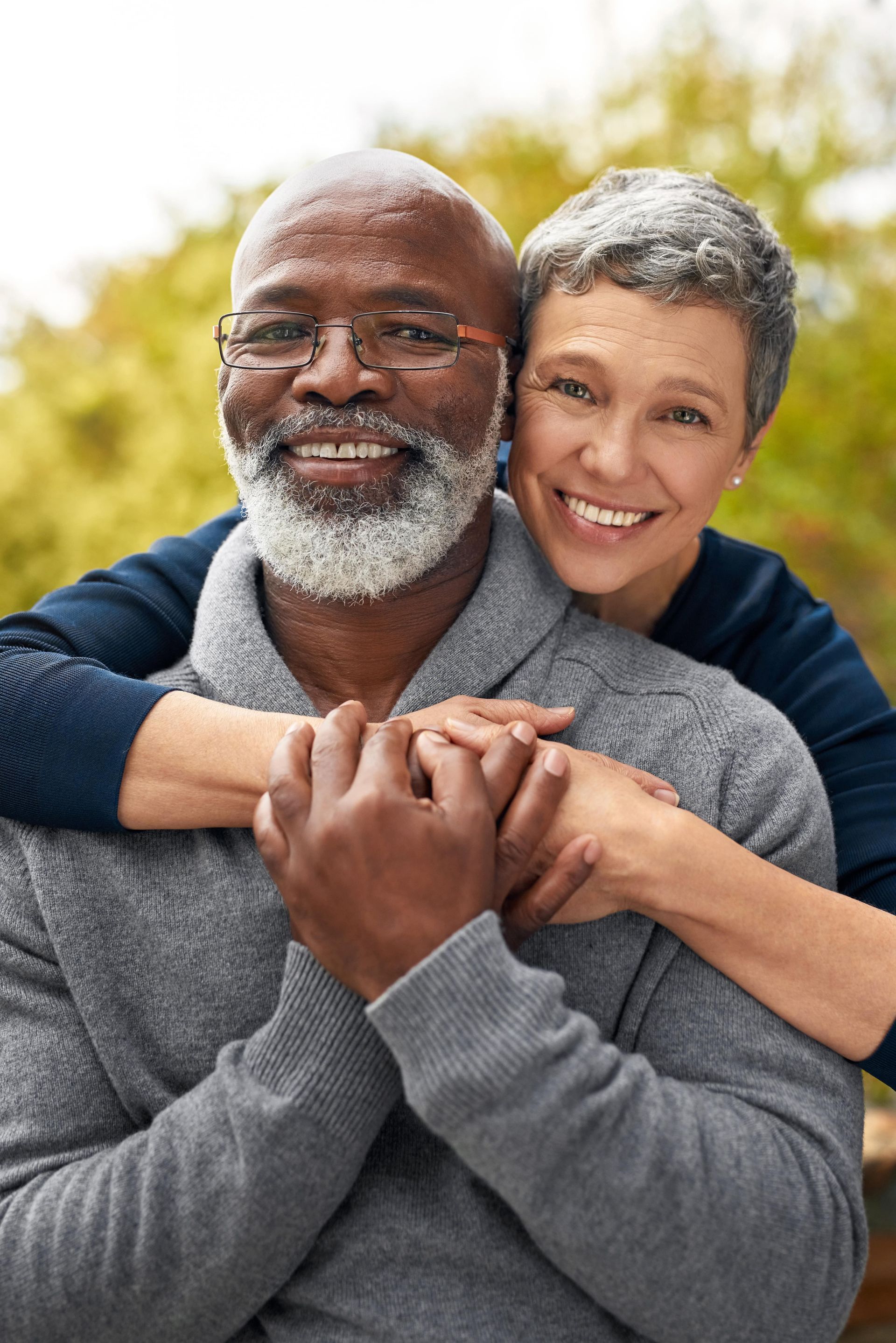 A woman is hugging a man from behind and they are smiling for the camera.