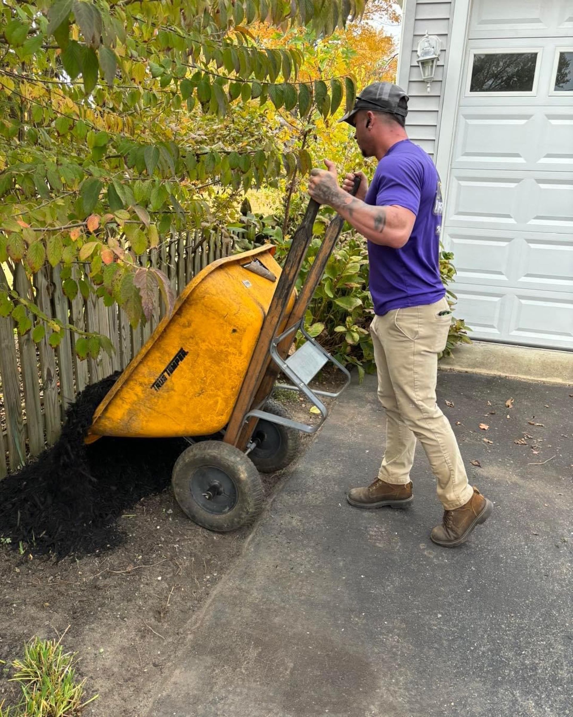 A man is pushing a yellow wheelbarrow full of mulch.