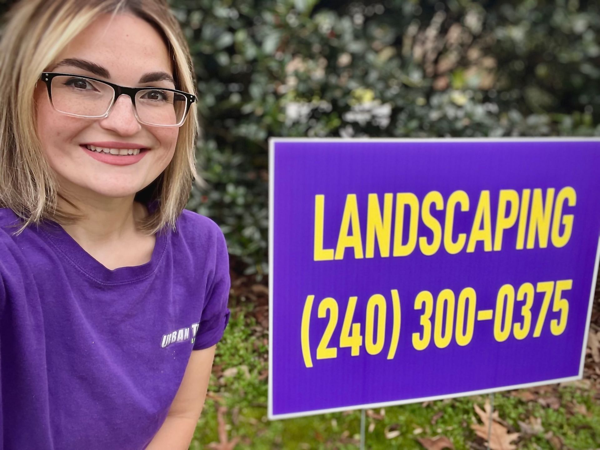 A woman is standing next to a sign that says landscaping