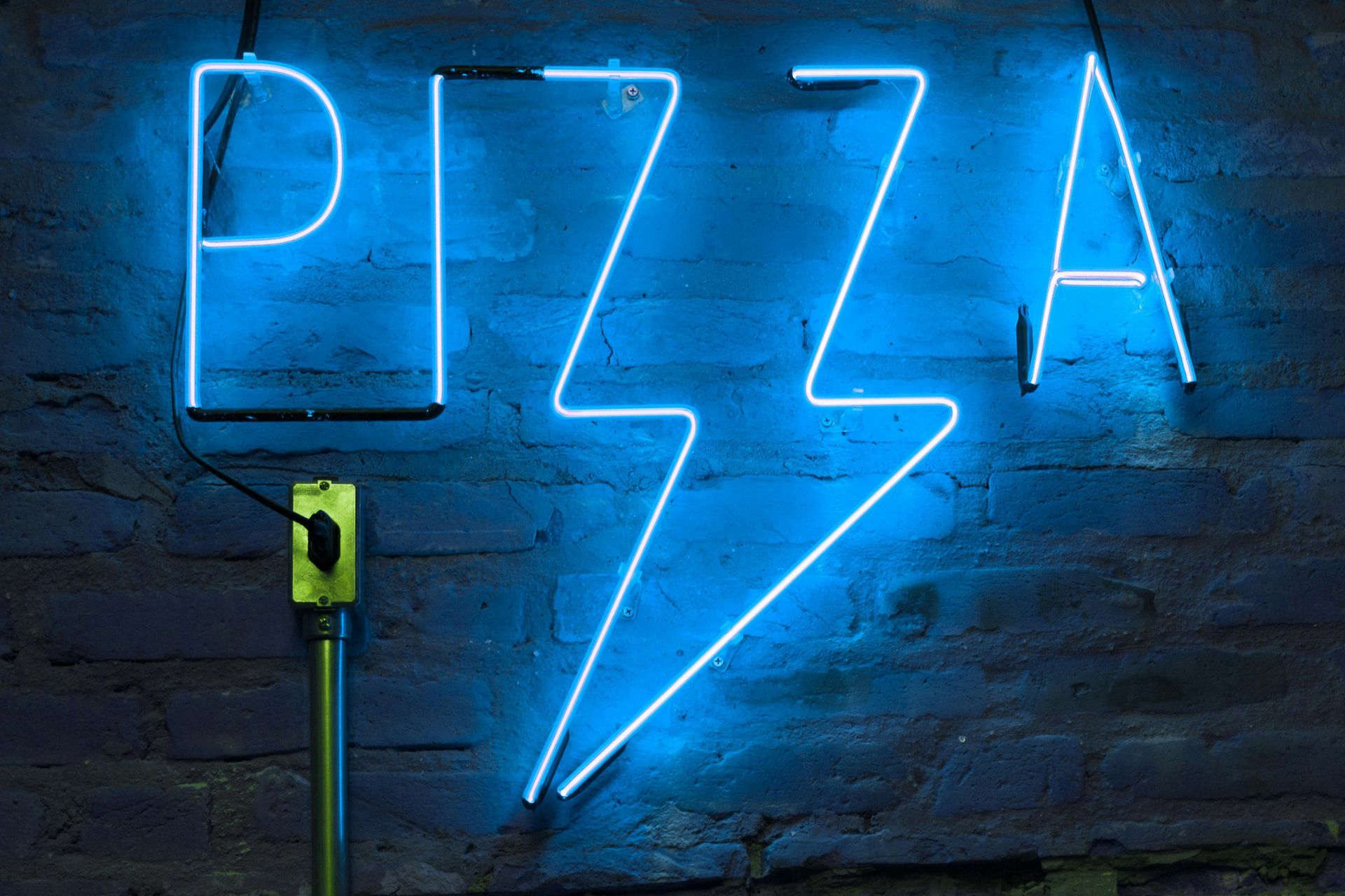 A neon sign that says pizza on a brick wall.