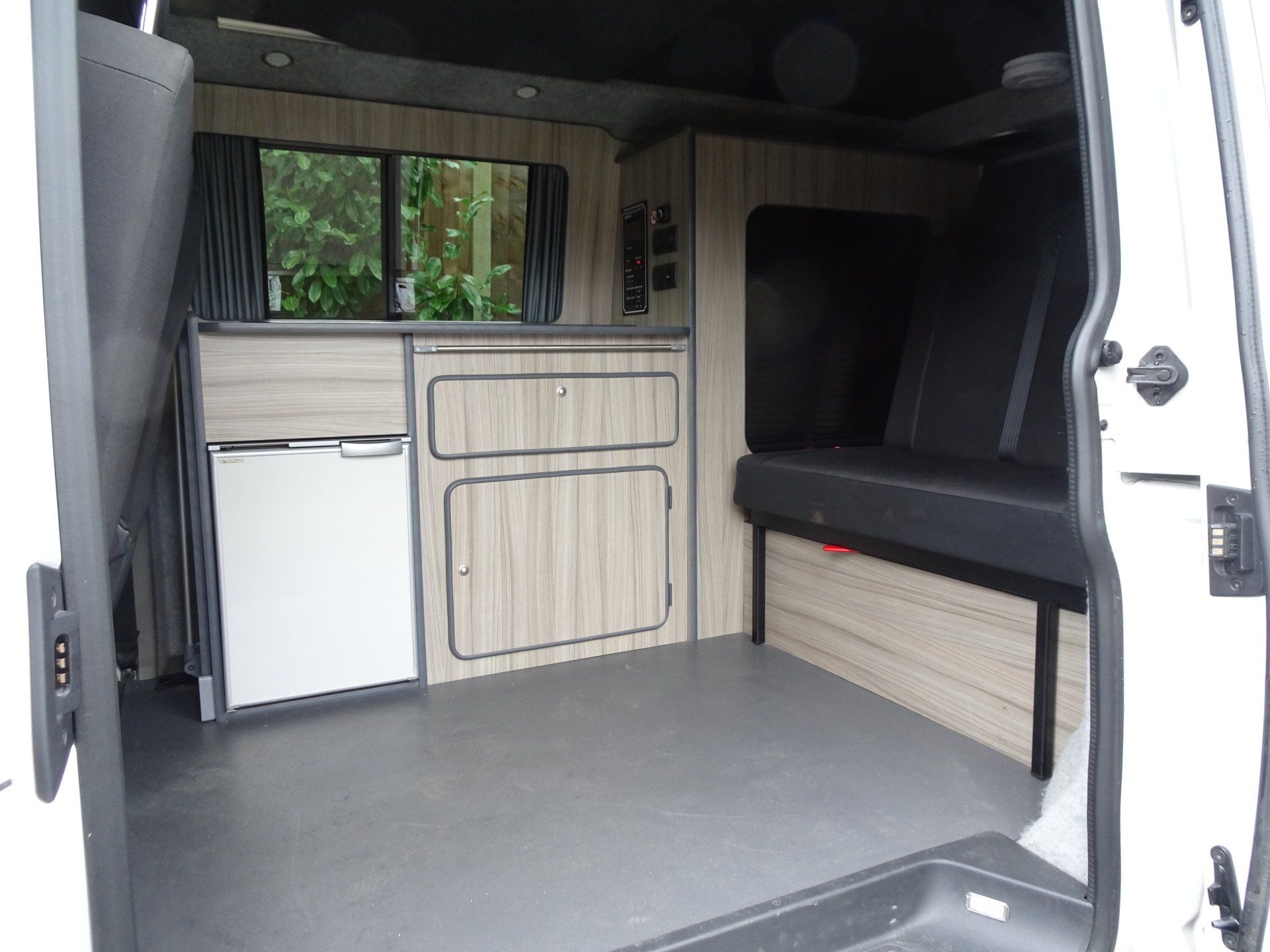 The inside of a white van with wooden cabinets and a refrigerator.