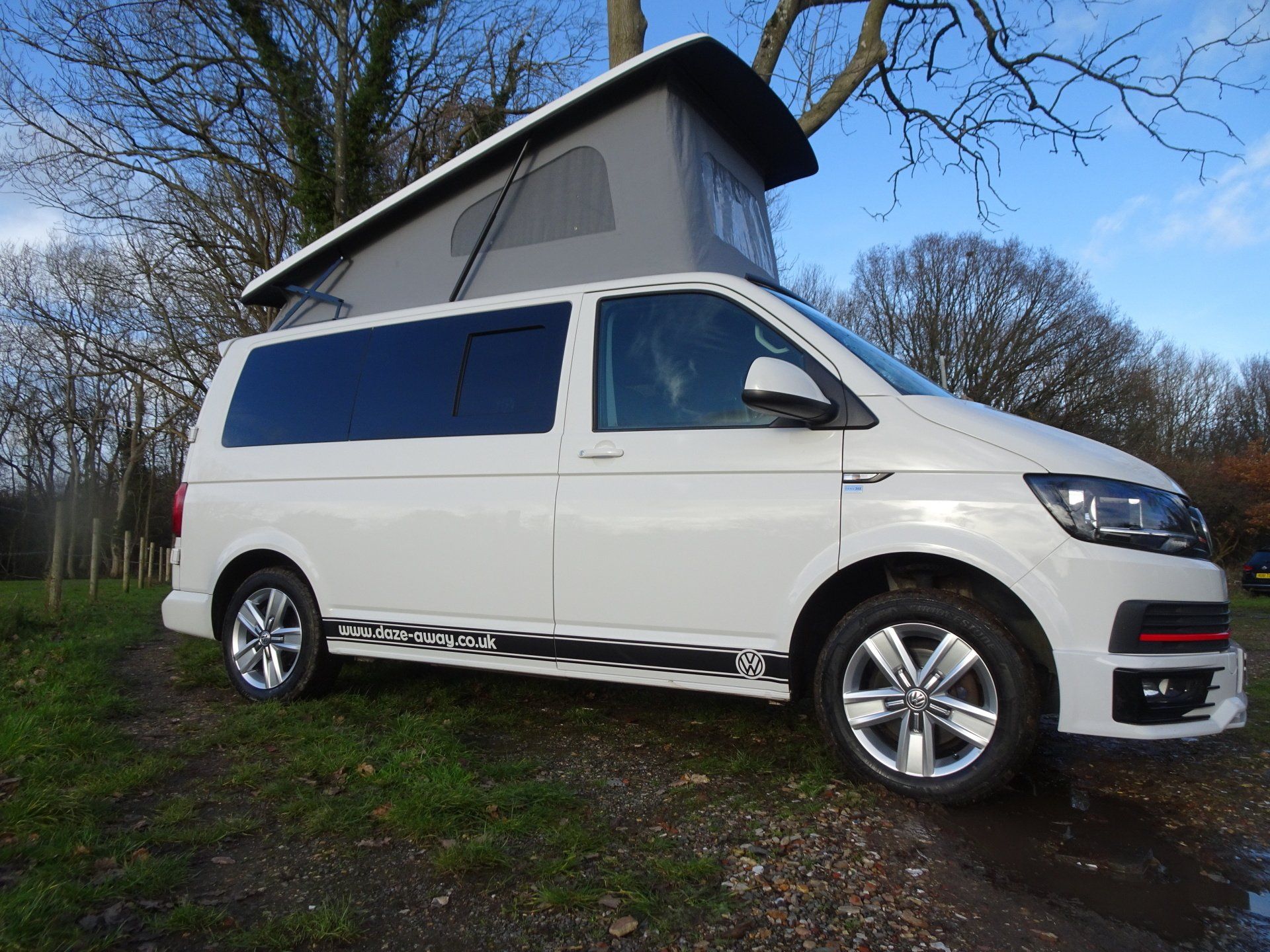 A white van with a pop up roof is parked in a field.