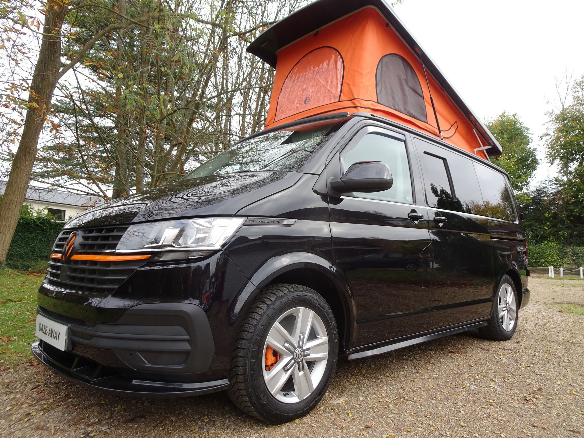 A black van with an orange tent on top is parked on a gravel road.