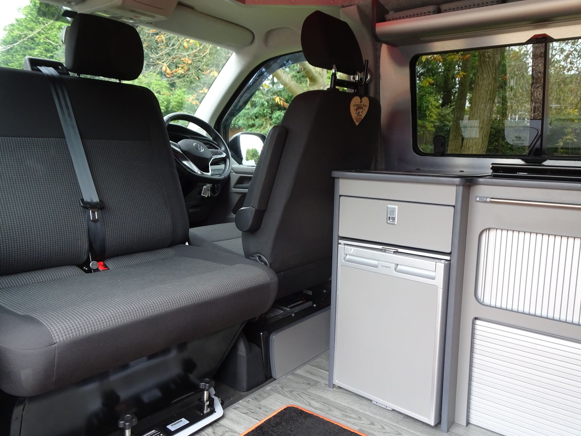 The inside of a van with two seats and a fridge.