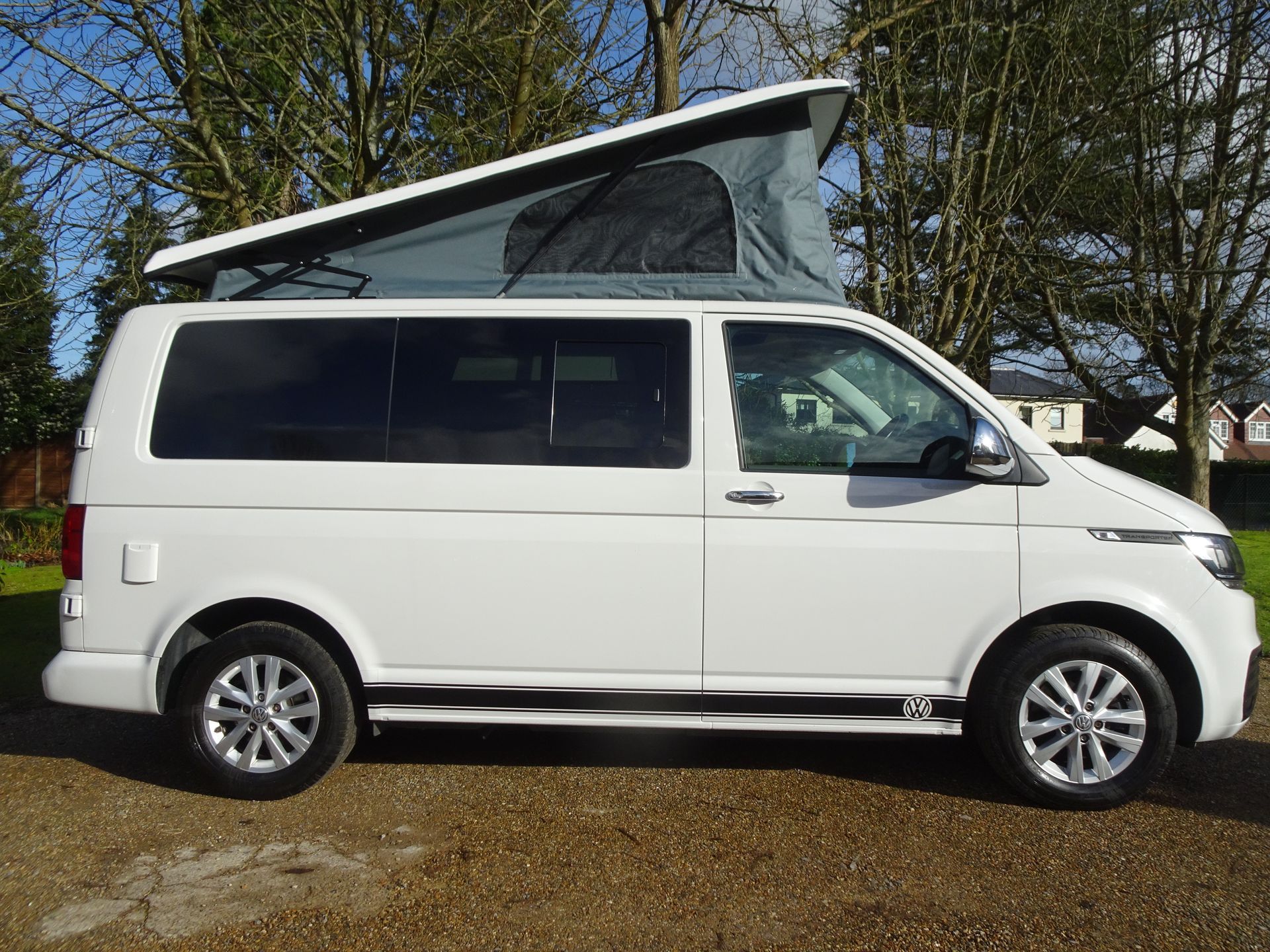 A white van with a pop up roof is parked in a driveway.