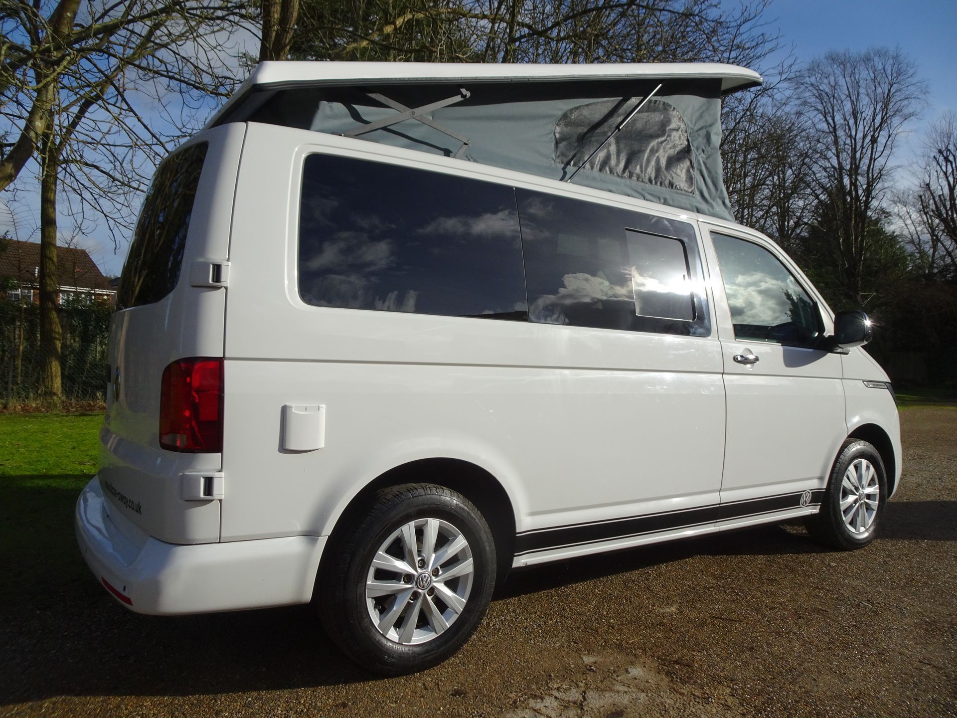 A white van with a pop up roof is parked in a driveway.