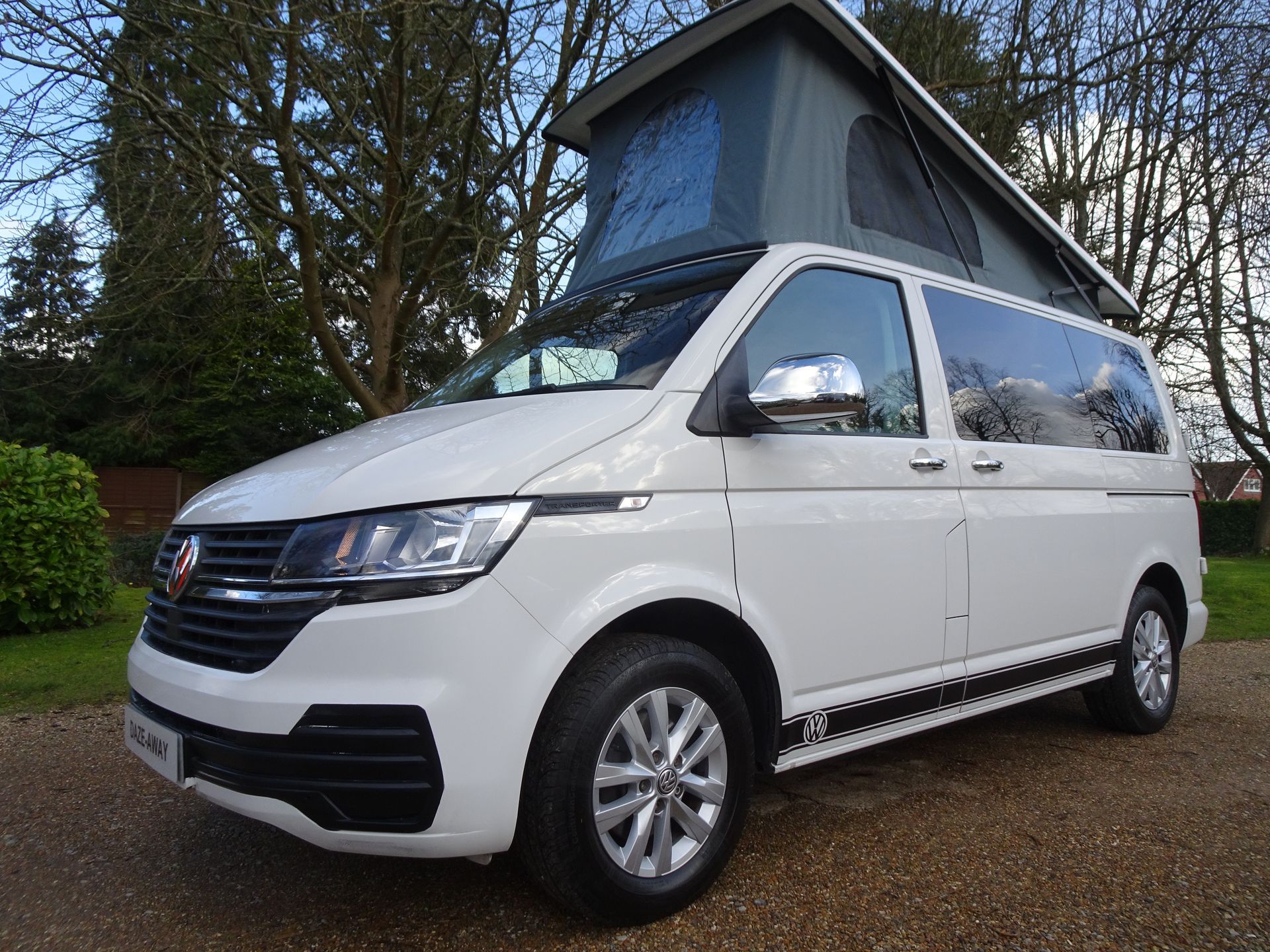 A white van with a pop top roof is parked in a driveway.