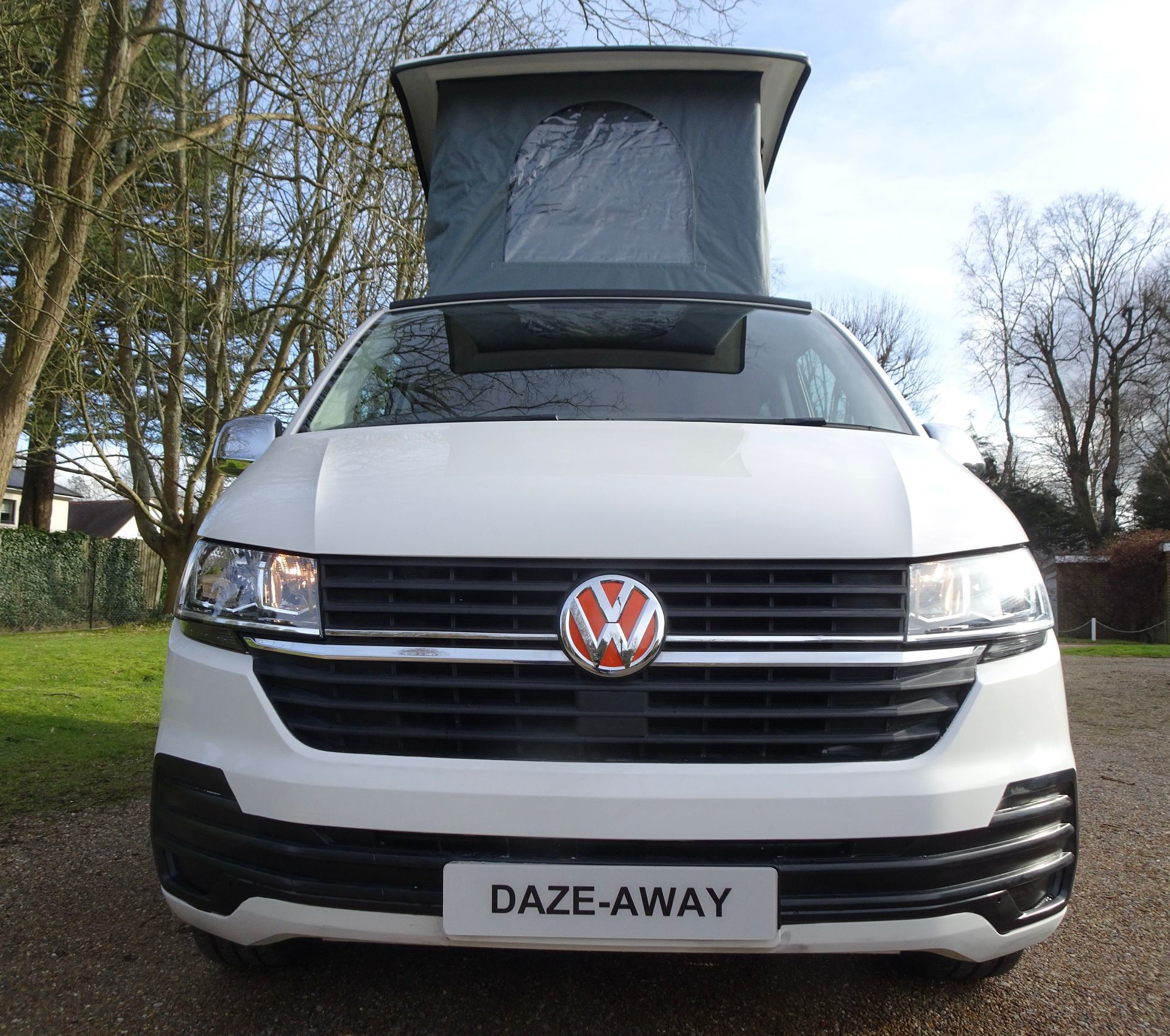 A white volkswagen van with a pop up roof is parked in a driveway.