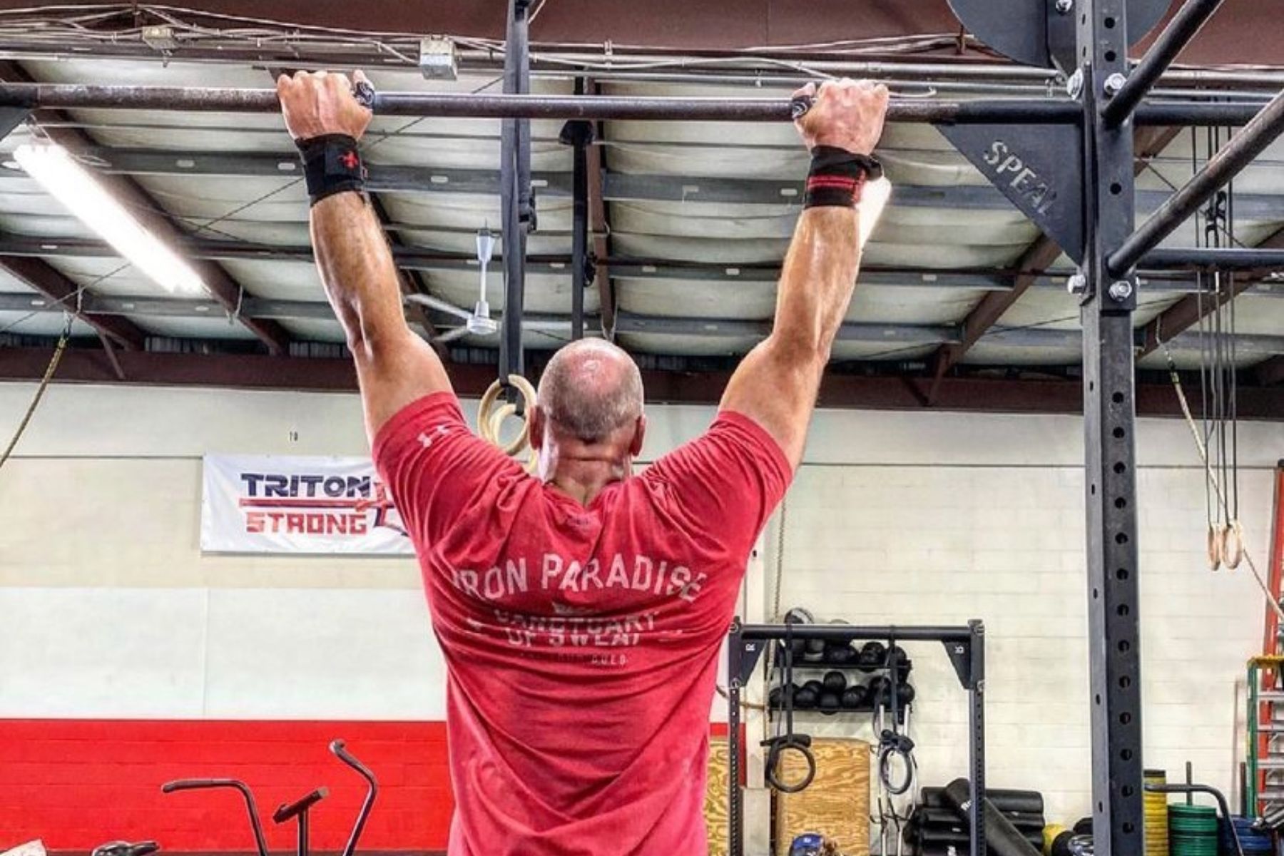 A man in a red shirt is doing a pull up in a gym.