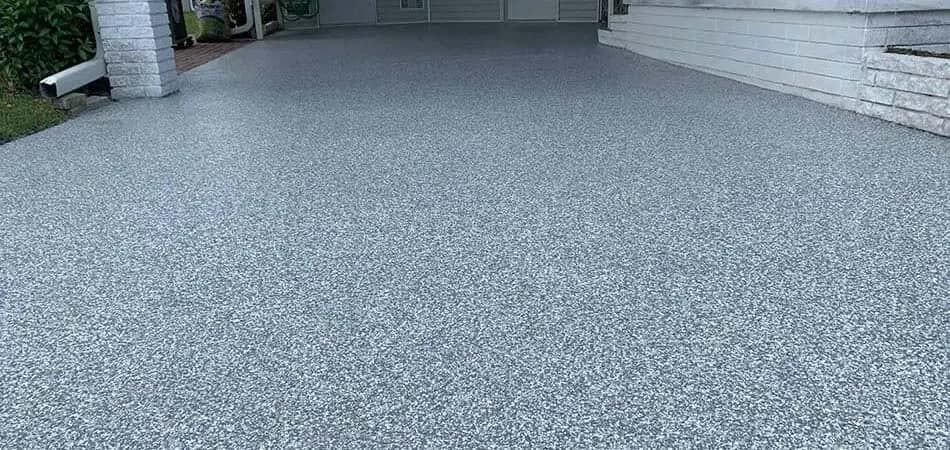 A grey gravel driveway leading to a garage. A white brick column is on the left.