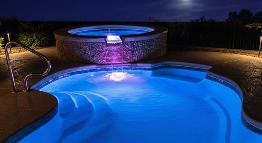 Pool and hot tub illuminated at night, with blue and purple underwater lights.