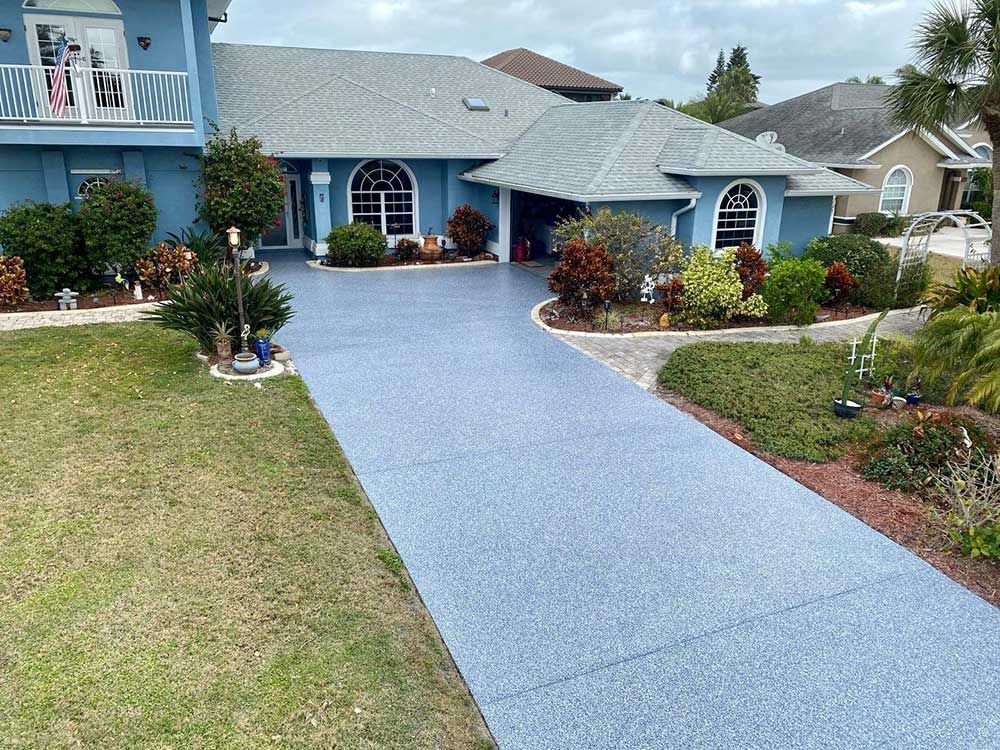 Blue house with a light blue driveway, surrounded by green grass and landscaping.